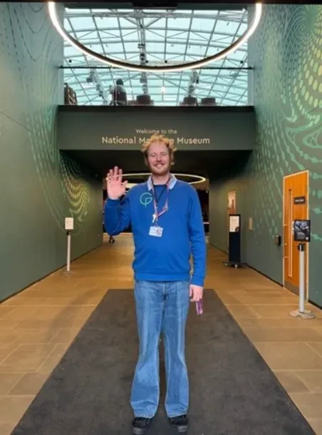 A Visitor Services Assistant in blue uniform waving to the camera in the entrance of the museum