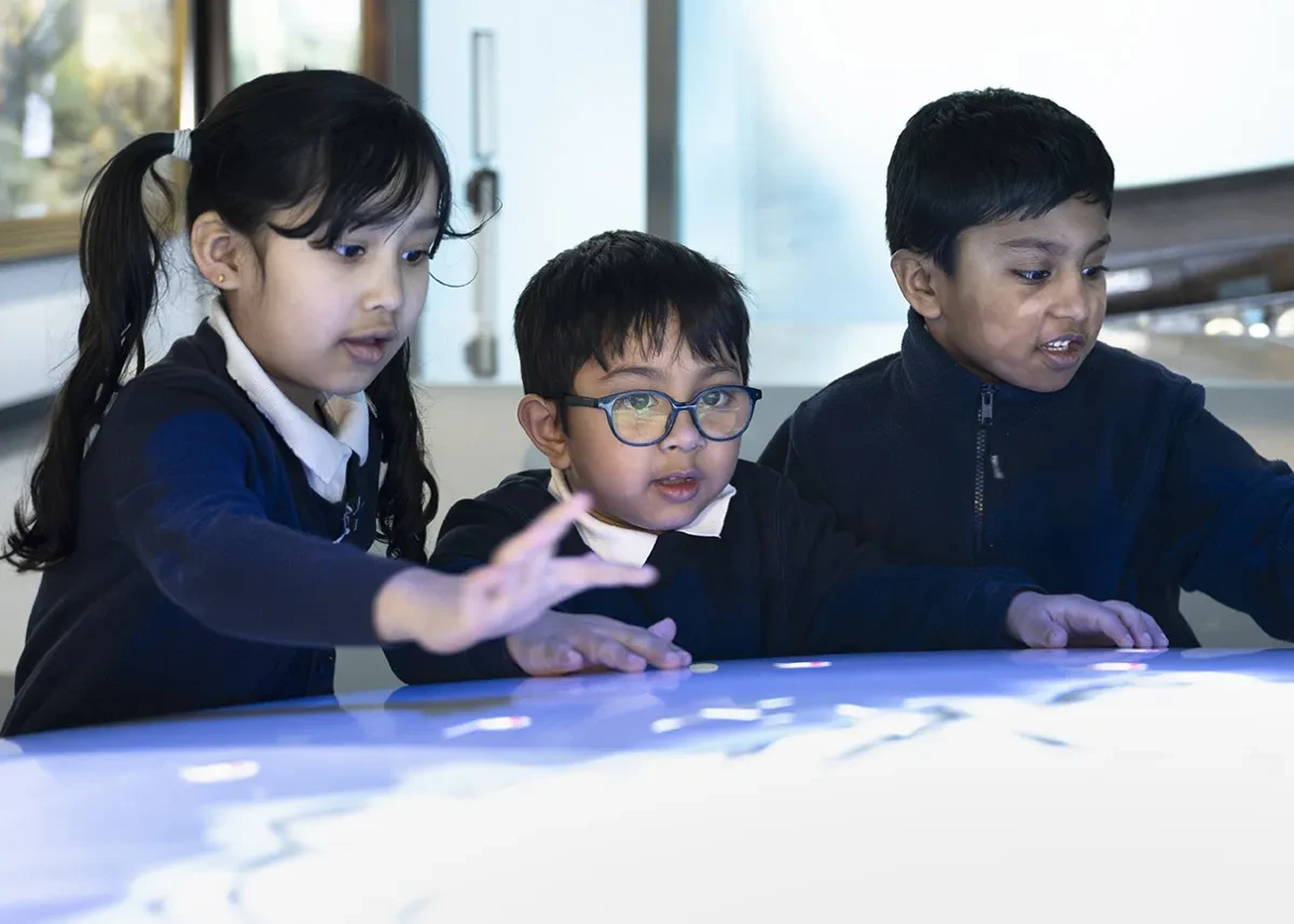 Three schoolchildren are fascinated by a light-up map of the polar regions.