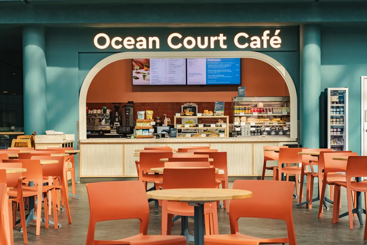 A cafe with coral-coloured seats and wooden-topped tables with a white counter and blue walls