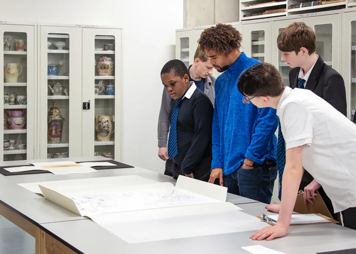 A group of schoolchildren and a teacher look at manuscripts in a museum store.