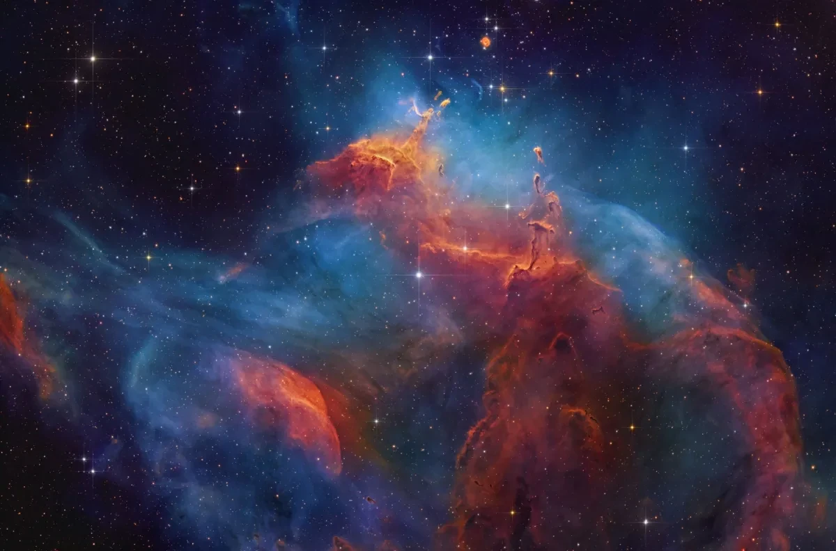 Blue, red and orange dusty shapes float in a black sky dotted with stars