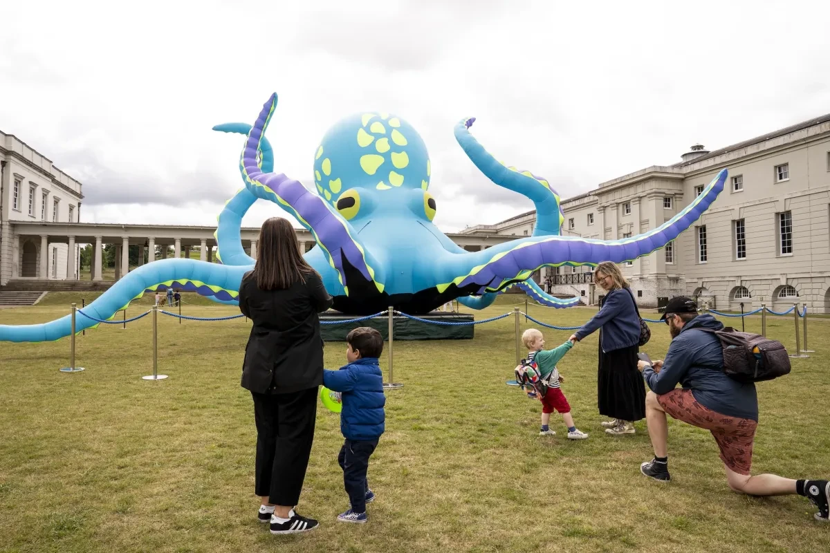A group of adults and children stand looking at a giant blue inflatable octopus