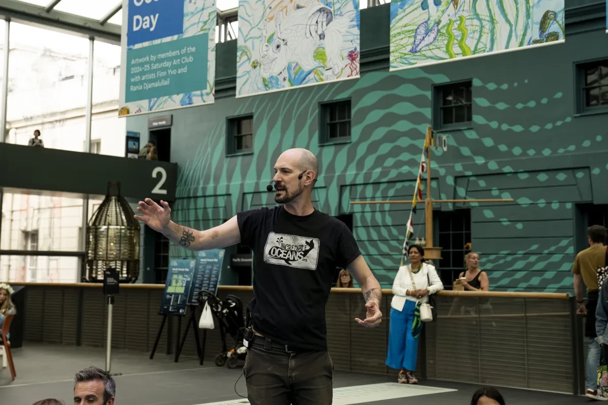 A man wearing a small microphone gives a talk in the middle of the National Maritime Museum