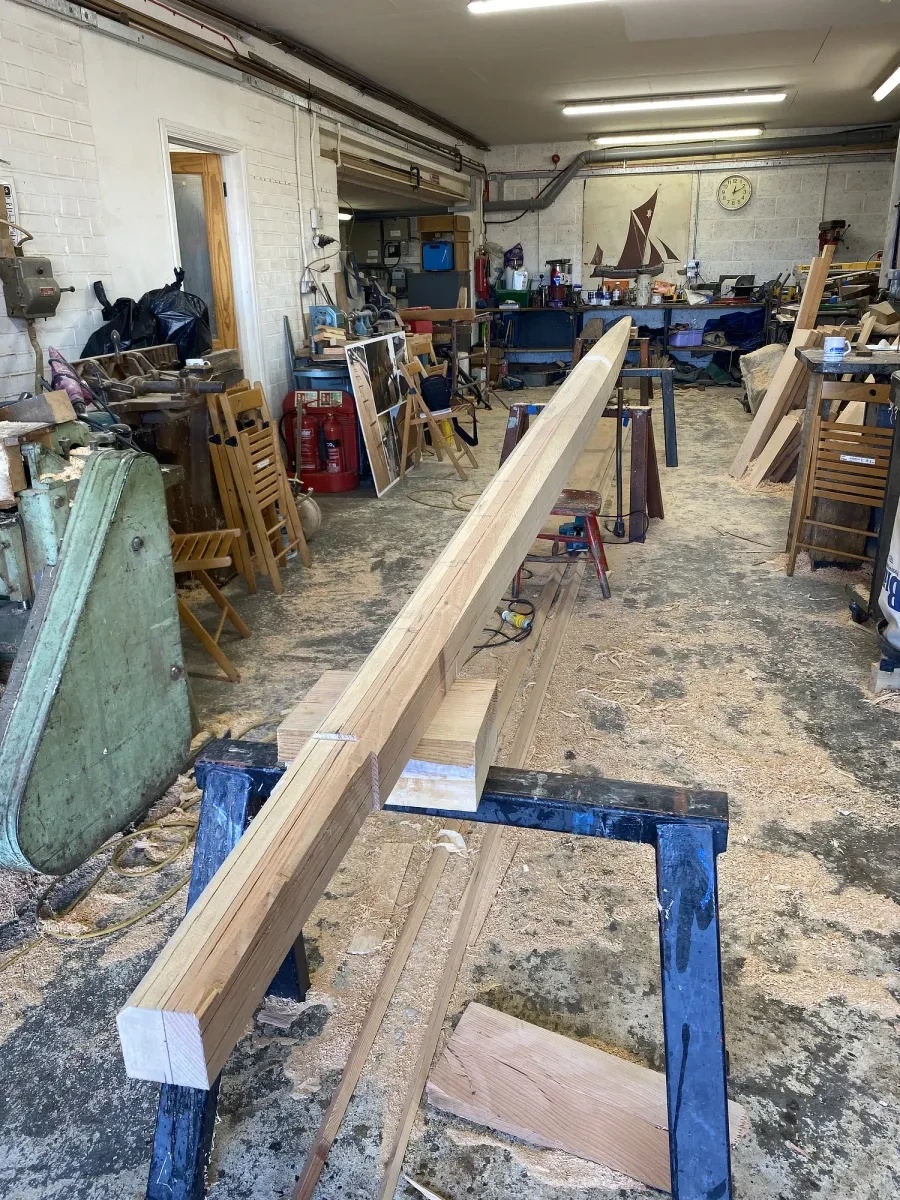 A wooden beam sits on a blue support in a shipwright's workshop