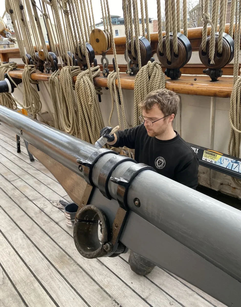 A shipwright paints a long beam grey