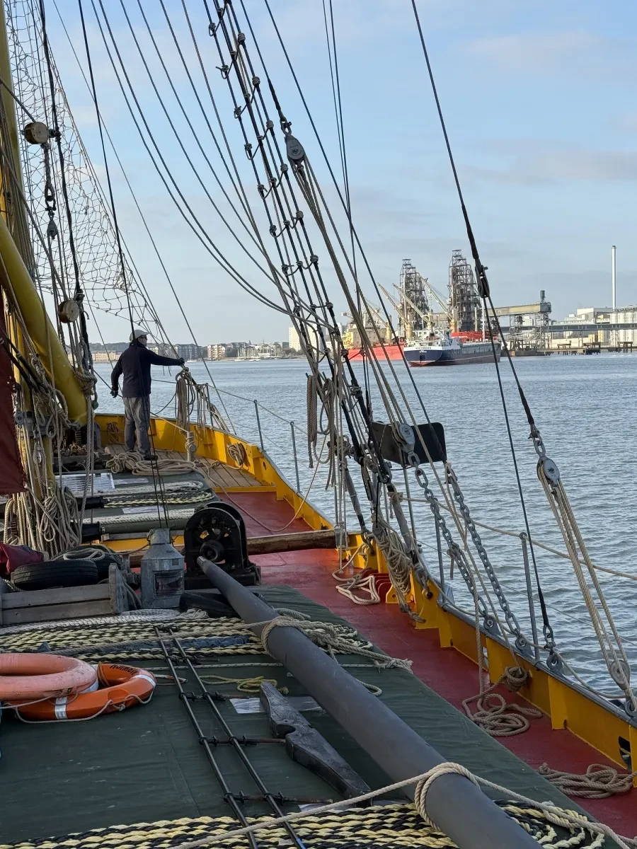 A black beam is tied to the deck of a ship, which is sailing on a busy river