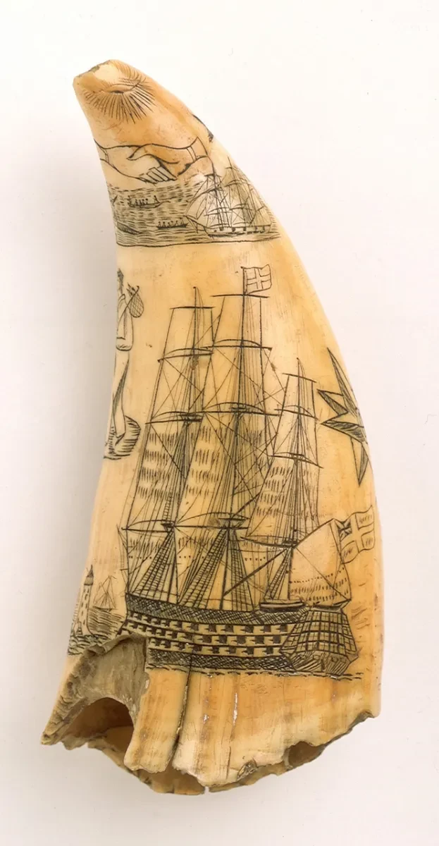 A sperm whale tooth engraved with a seated figure representing Britannia. Below, a sailor is shown parting from his girl. On the other side, is a warship and a lighthouse flanked with a star and a sailor carrying a bundle on a stick over his shoulder. A whaling scene is placed above, beneath the Masonic symbols of clasped hands and a rayed eye.