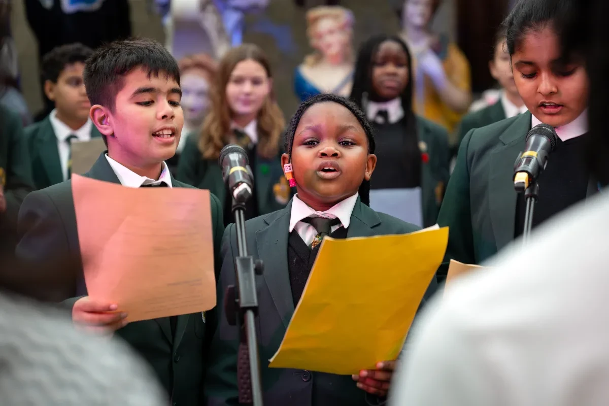 A group of children in school uniform singing into microphones.