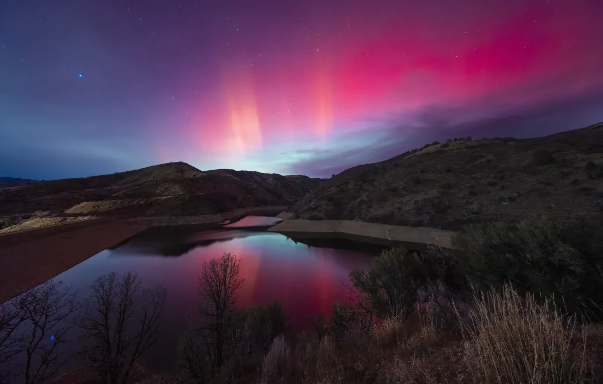 Photo showing dark reservoir with pink aurorae in the sky above