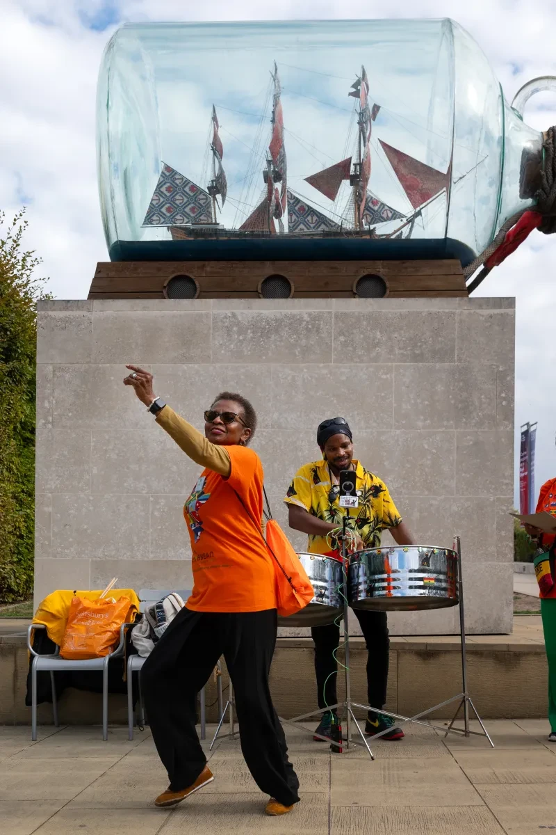 Two people dance in front of a statue of a ship inside a glass bottle