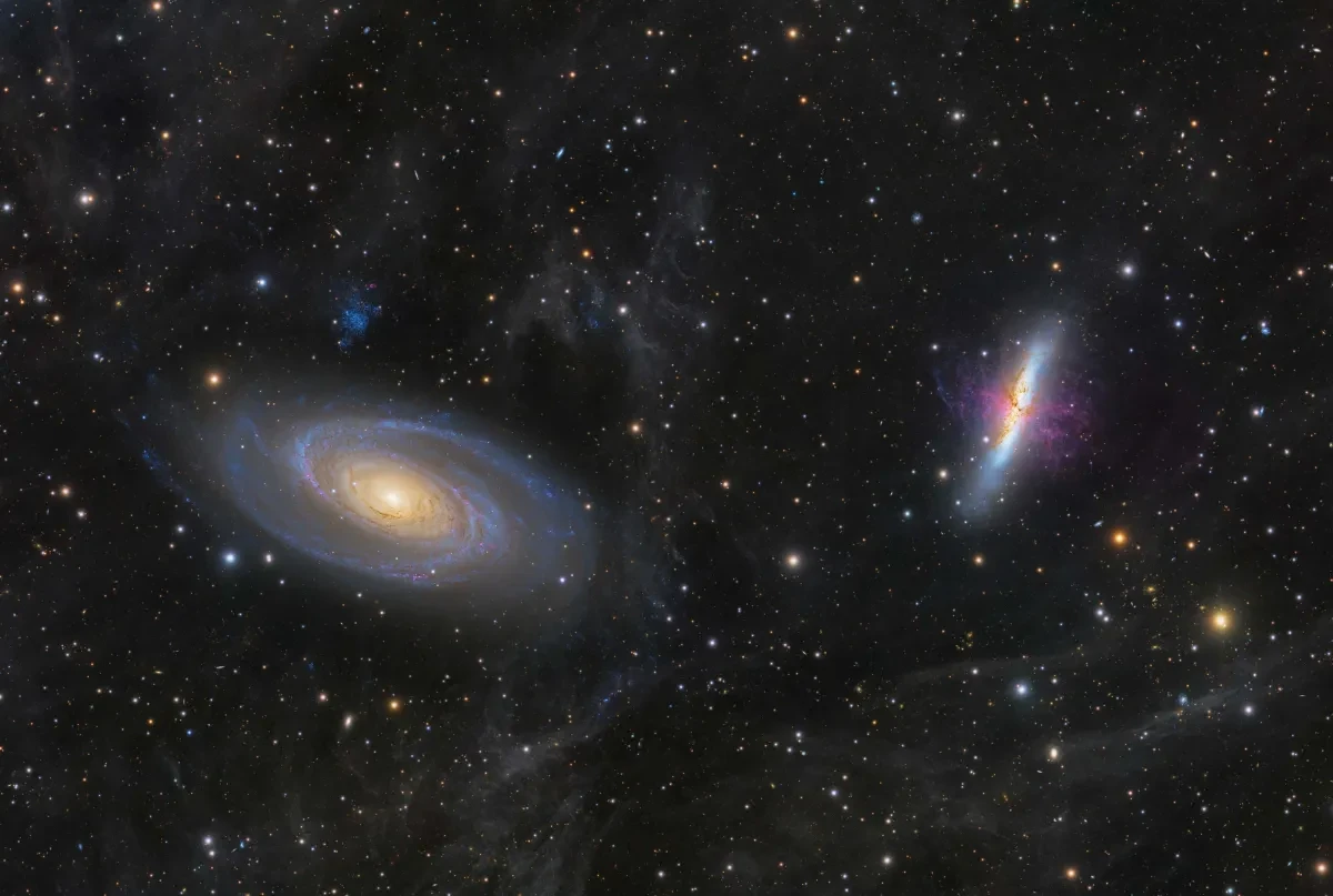 Two galaxies in a starry night sky, one on the left a spiral galaxy with light blue spiral arms, and the one on the right a vertical blue column with a purple vein-like structure over it