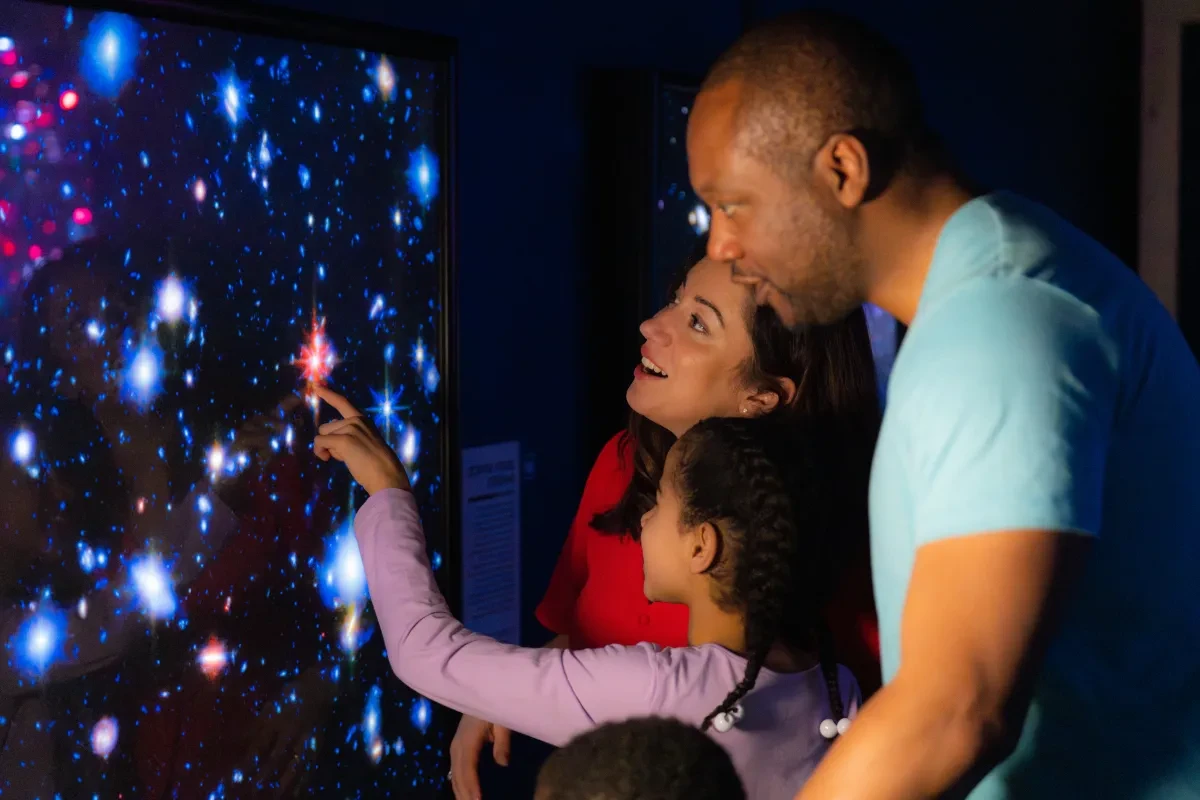 A family in bright clothes smile as they look at the lightbox images of stars in Astronomers' Take Over at the National Maritime Museum