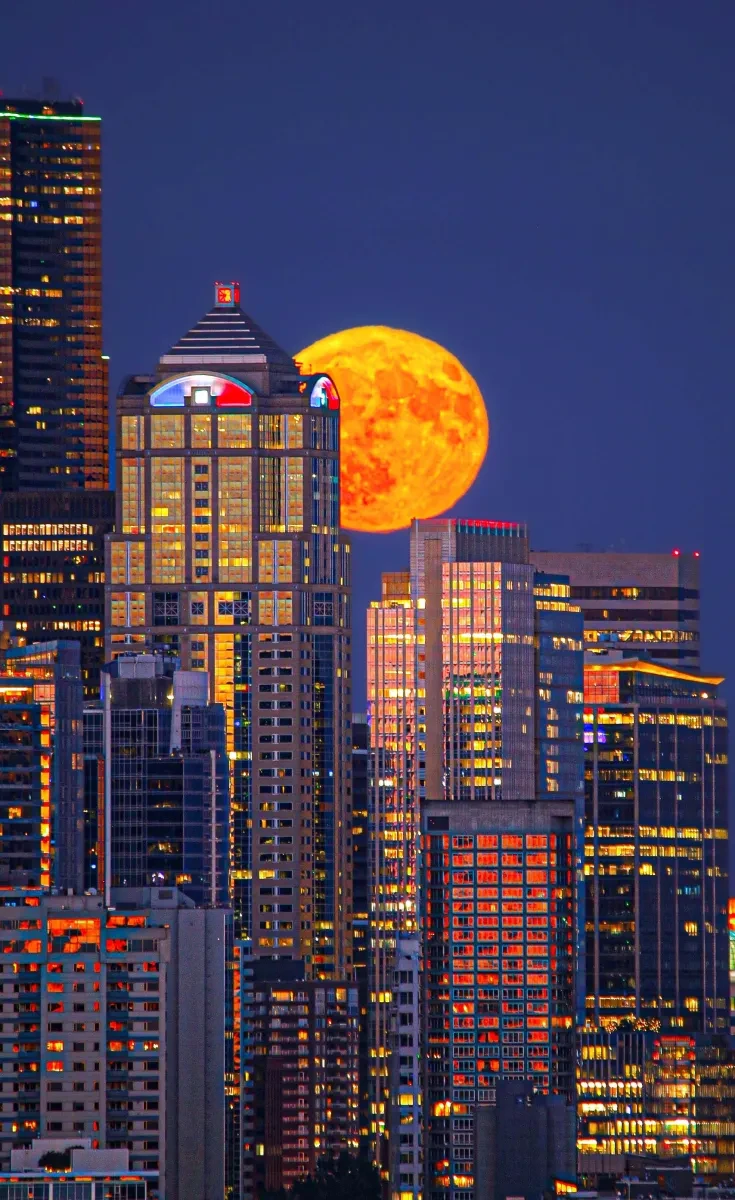 Photo of city skyline with big orange moon behind skyscrapers