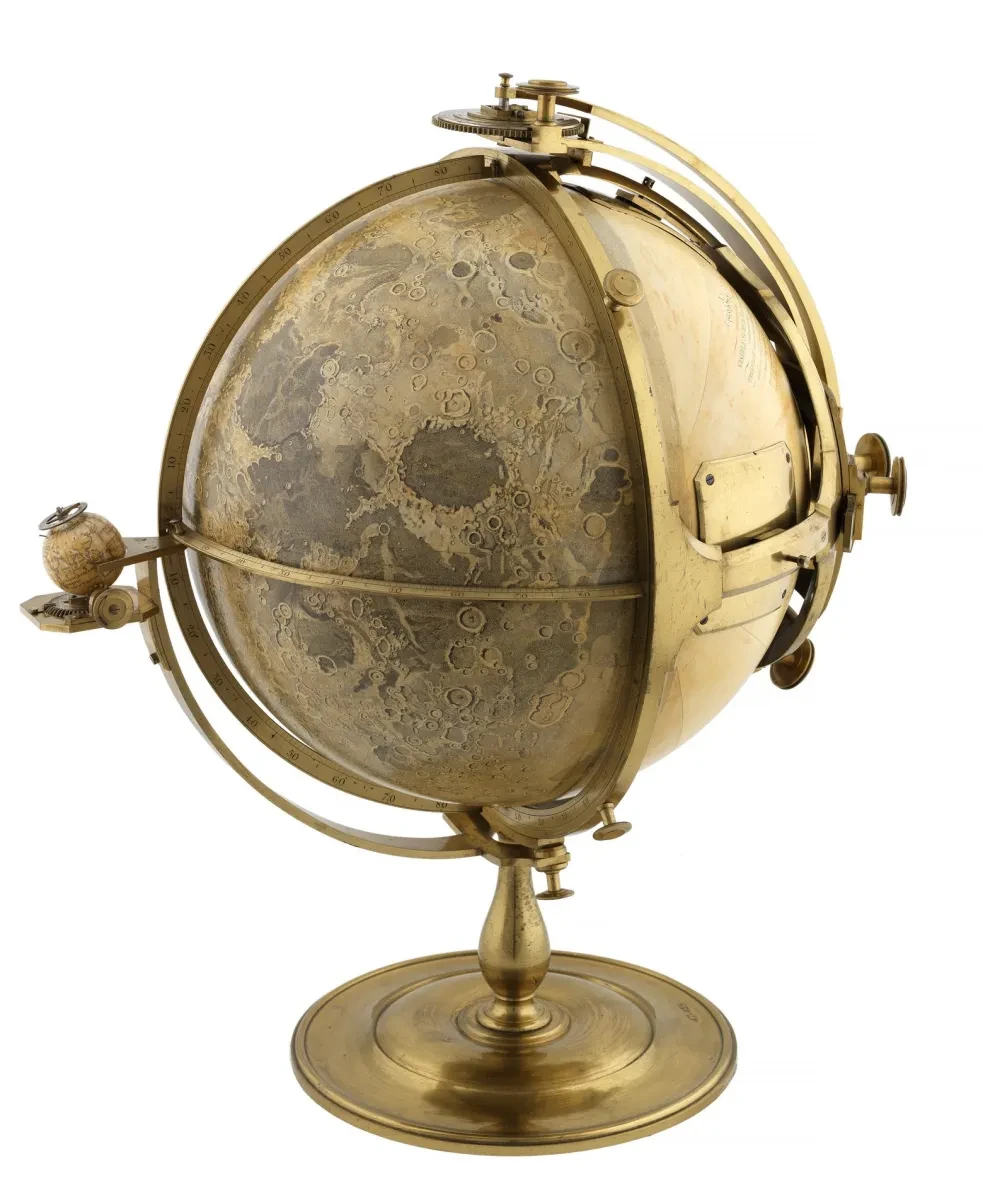 A golden globe model of the Moon on a stand with a mechanism around it and a tiny globe representing Earth on the left