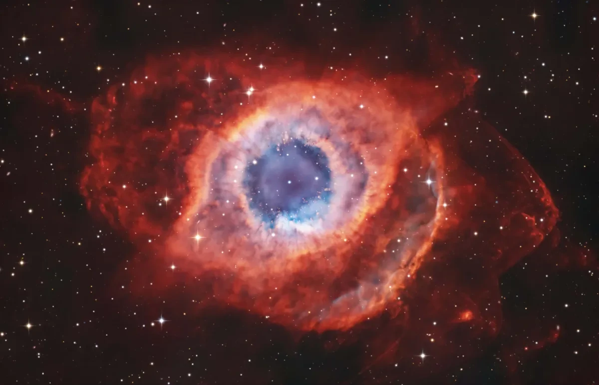 Bright nebula that resembles an eye, with a green ringed pupil and surrounding oval-shaped clouds in varying shades of red