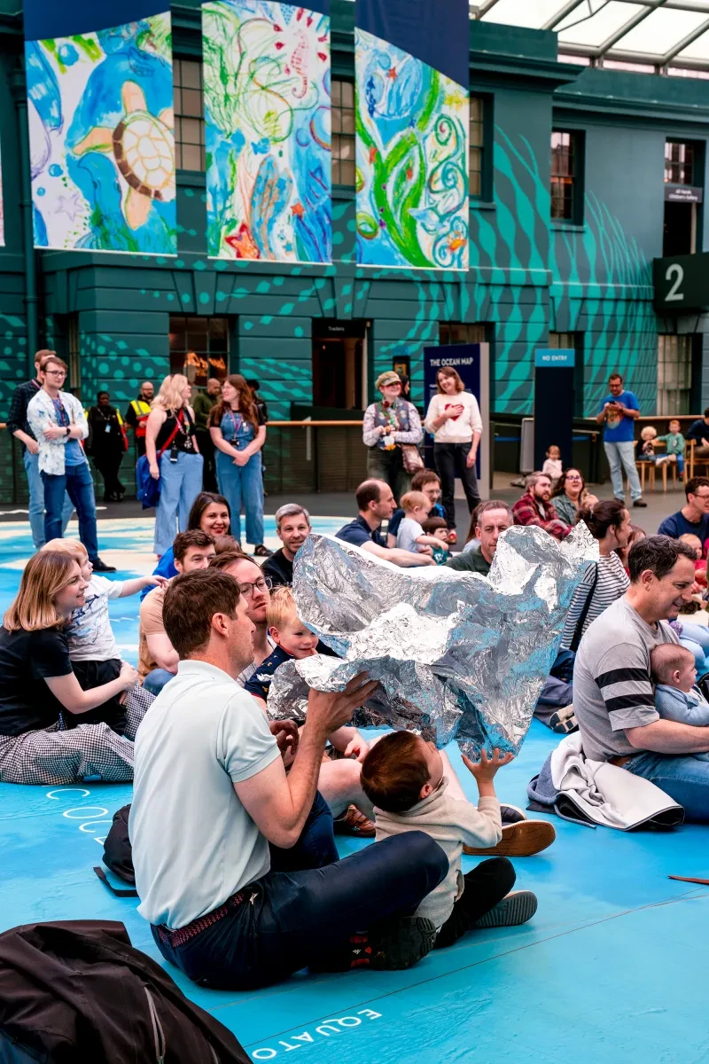 A group of children with their parents play with a large piece of tinfoil during a performance inside the National Maritime Museum