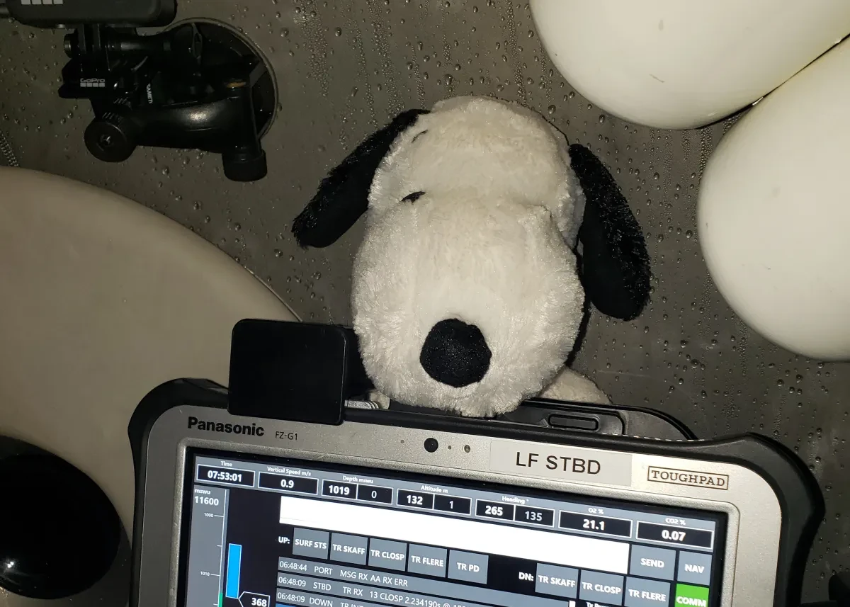 A soft toy Snoopy positioned above a submersible status panel during a deep-sea dive