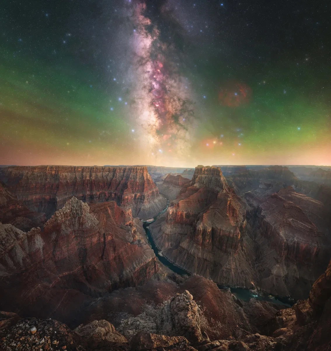 An expanse of red, white and grey stars and nebulae appears in a grey, green and light yellow sky above a rocky canyon in the lower half of picture. Part of the ZWO Astronomy Photographer of the Year competition 2026