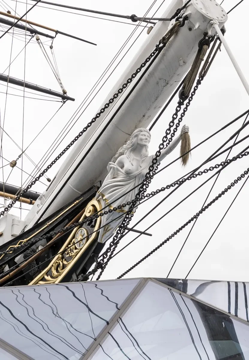 Figurehead for historic ship Cutty Sark which is a carved witch holding a horse's tail in an outstretched arm  