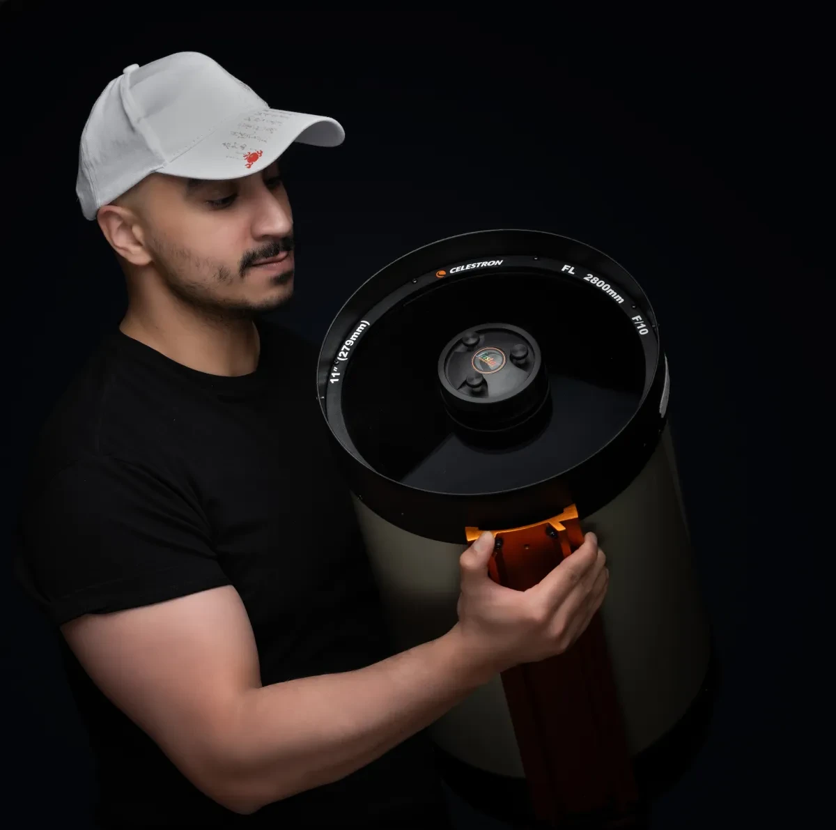 Photo of Ali Alobaidly wearing a hat and adjusting a large telescope