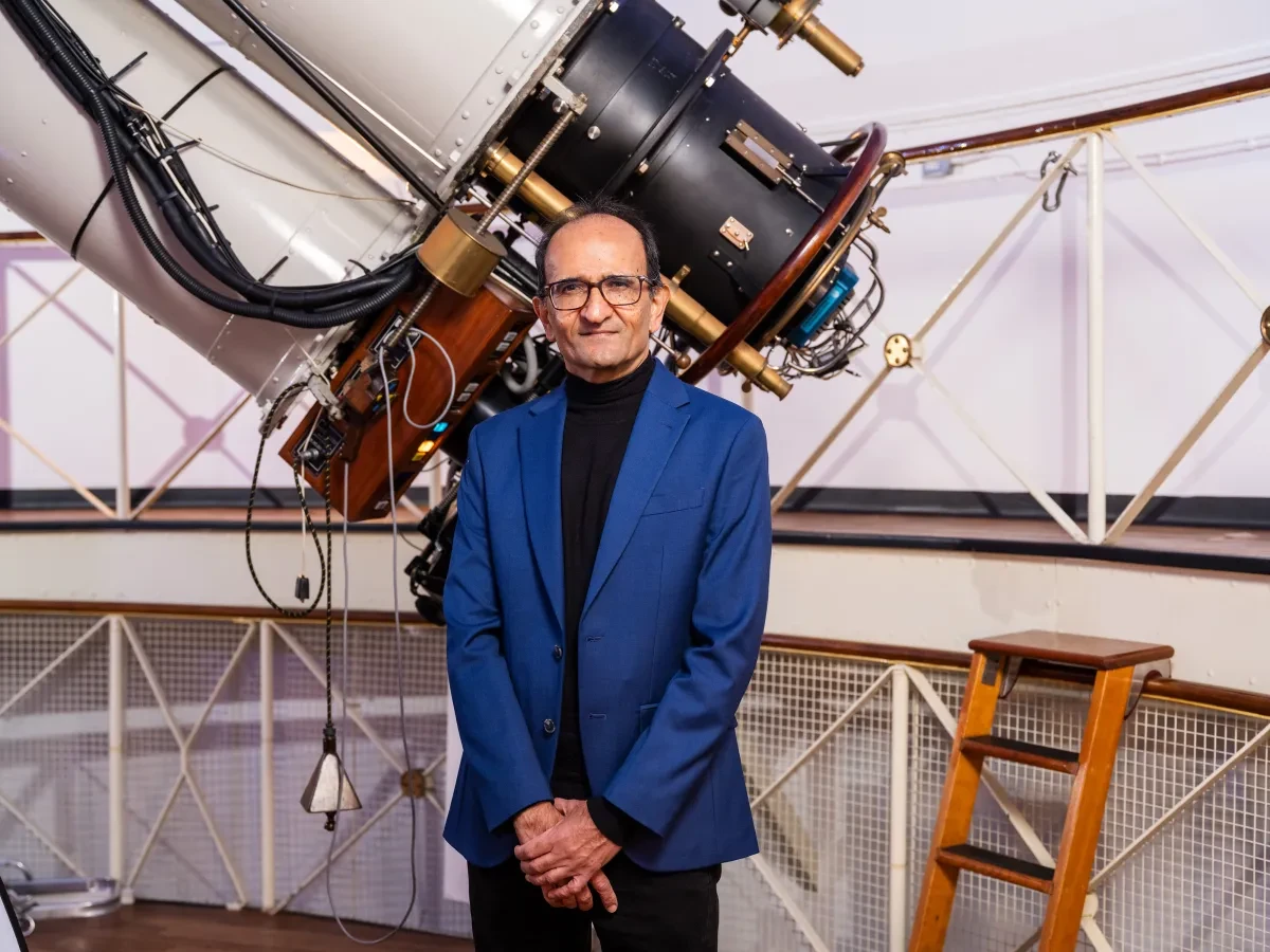 Man wearing blue suit standing in front of large telescope 