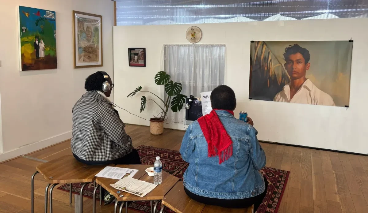 photo of two black women with their backs to the camera, looking and listening to artworks hanging on the walls.