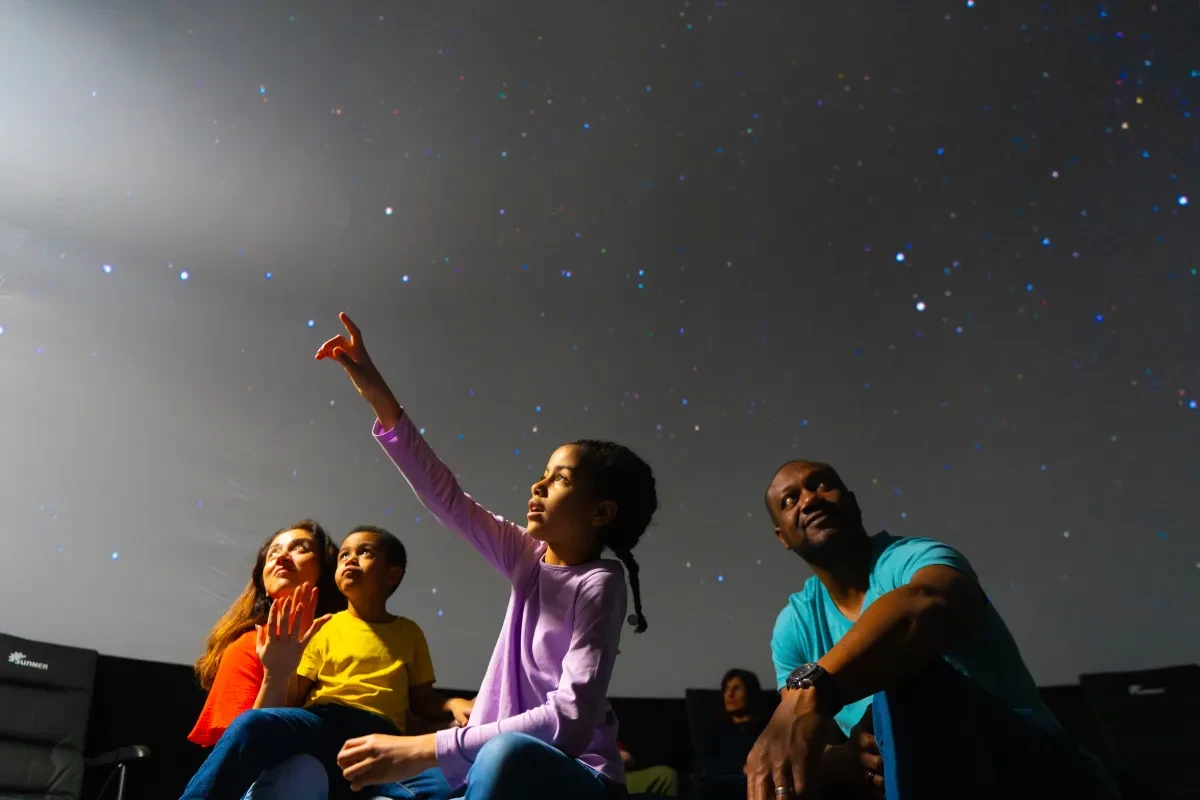 Family in planetarium looking up at starry sky with little girl pointing up in delight
