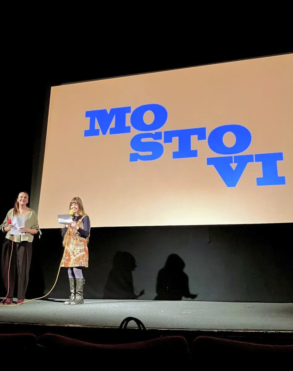 photo of 2 women stage to the side of a stage, with the backdrop of the film collective's name