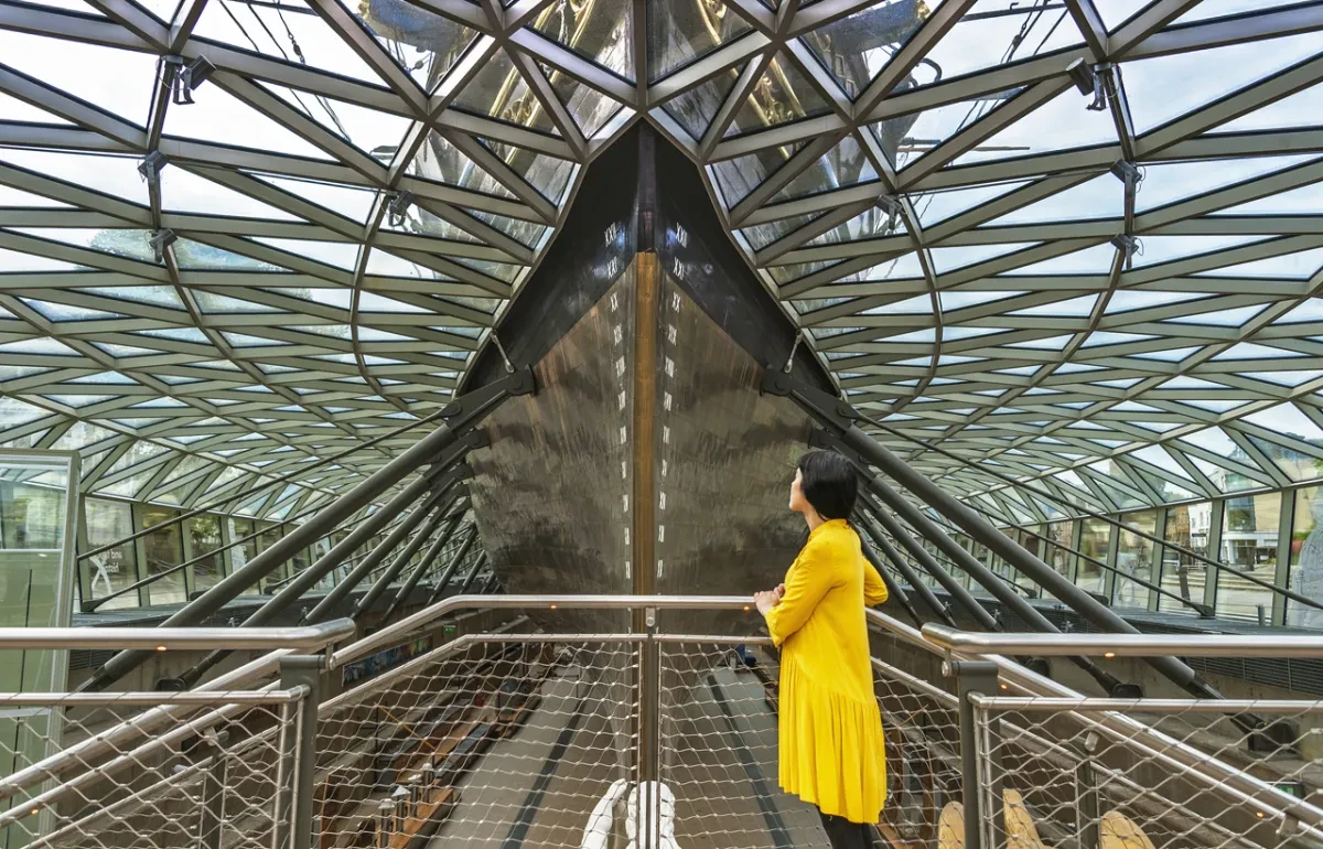 Visitor wearing a yellow jacket looks at Cutty Sark's hull