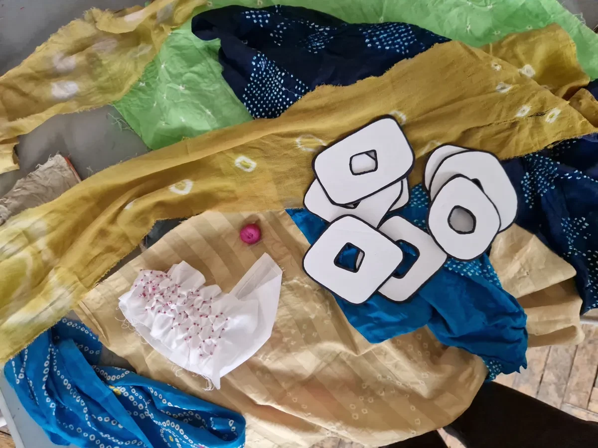 Pieces of yellow, blue and green fabric featuring Bandhani designs, with sewing materials and paper templates laid on top.