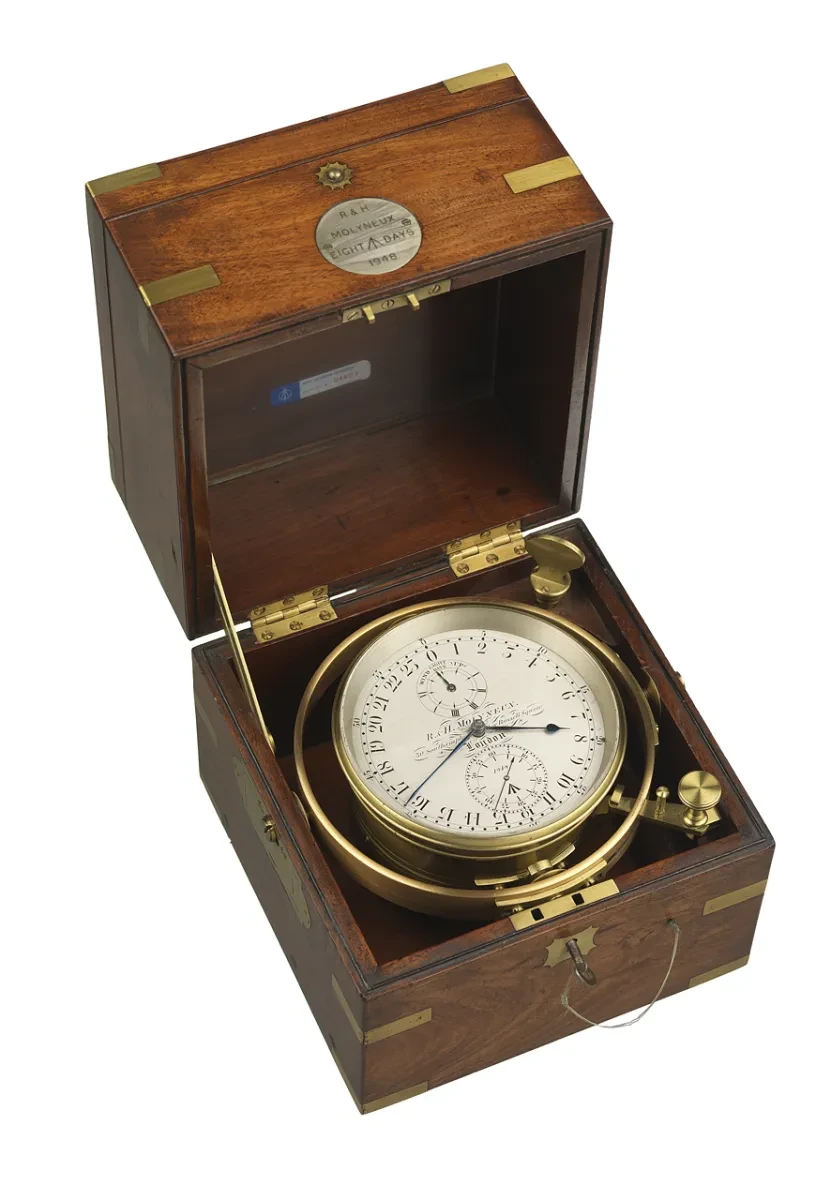 A gold-rimmed chronometer with a white face in a brown, wooden box