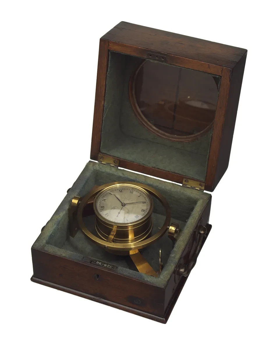A gold chronometer with a white face in a dark brown box
