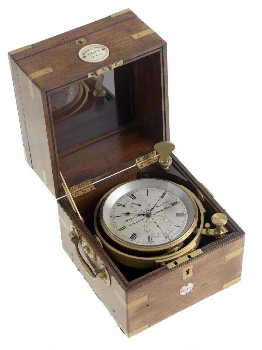 A white-faced chronometer in a brown wooden box