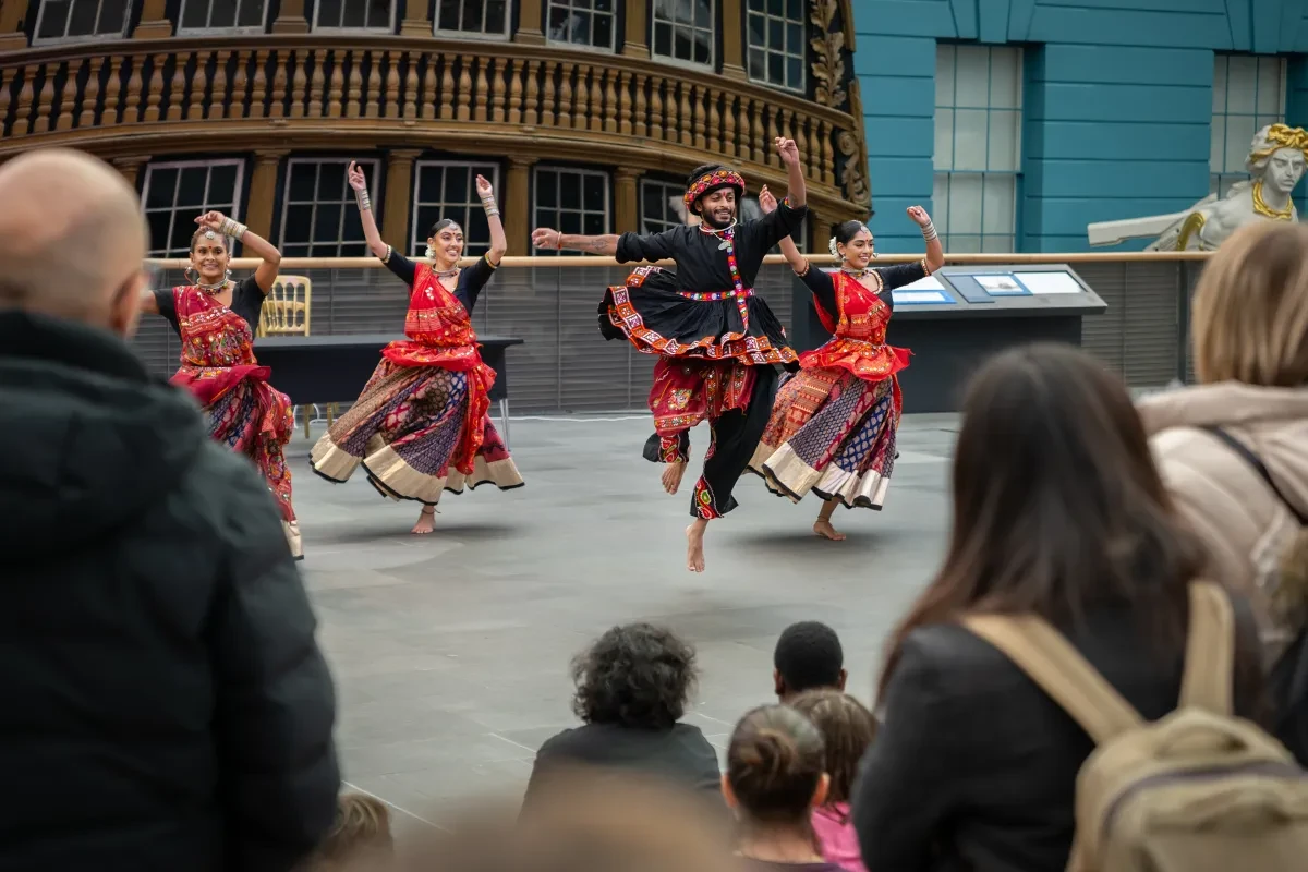 Four dancers in traditional red, black and gold dress dance on the Ocean Map at the National Maritime Museum's special Diwali event