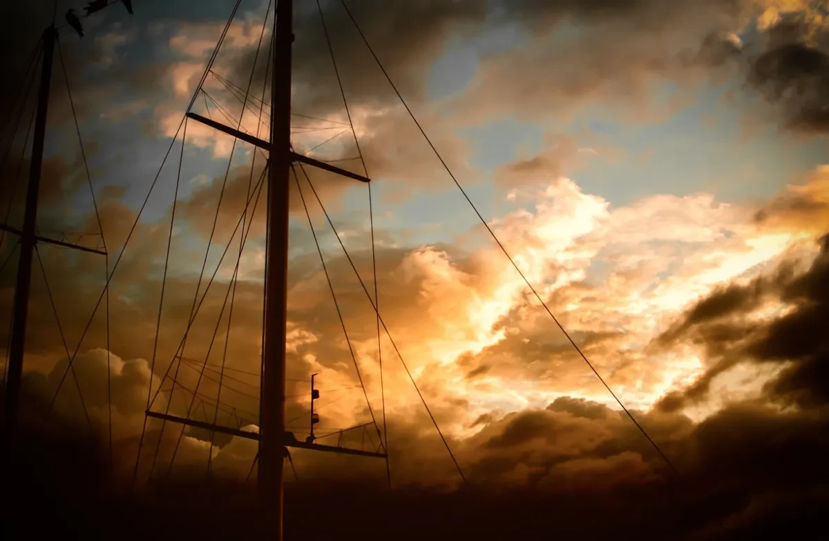 A ship mast silhouetted against a dramatic cloudy sunset.