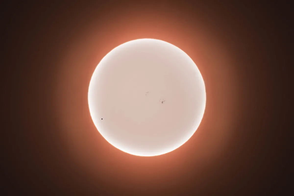 White Mercury is silhouetted against the Sun, with a red halo effect.