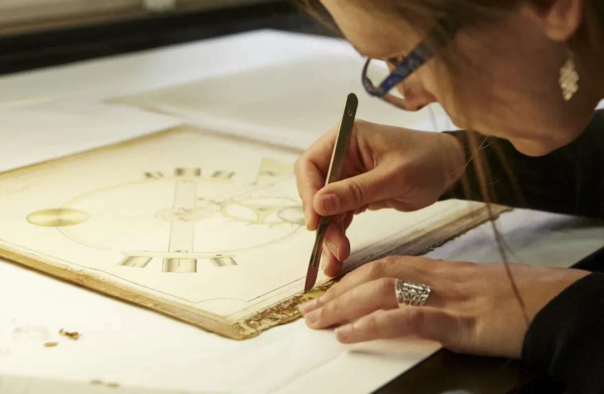 A conservator uses a scalpel on the edge of a paper item.