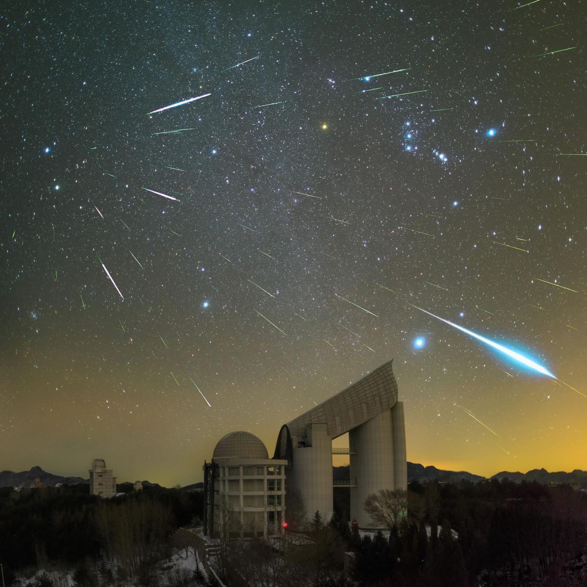 Image of meteor shower with around 30 meteors in the sky over a large observatory telescope