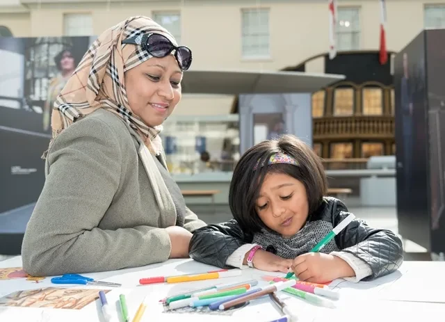 A mum watches as her child draws with coloured pens.