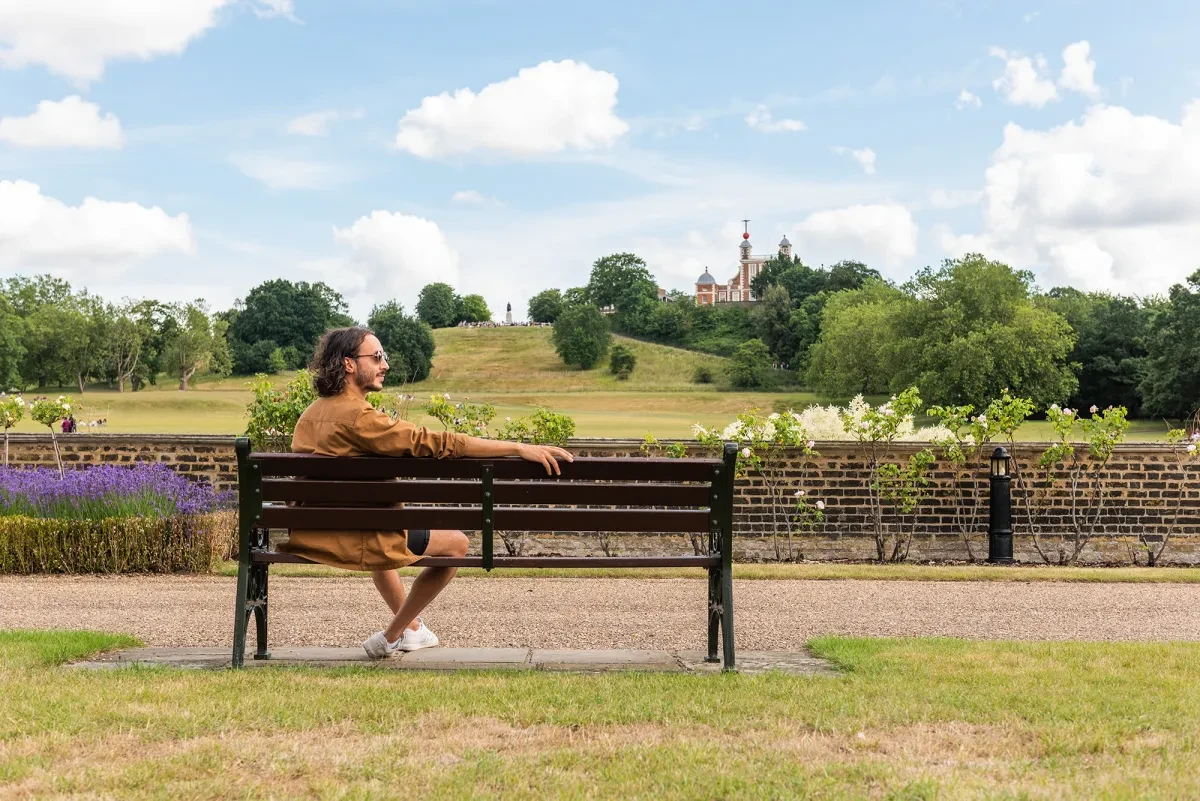A man sits on a bench, with Royal Observatory Greenwich in the distance..jpg