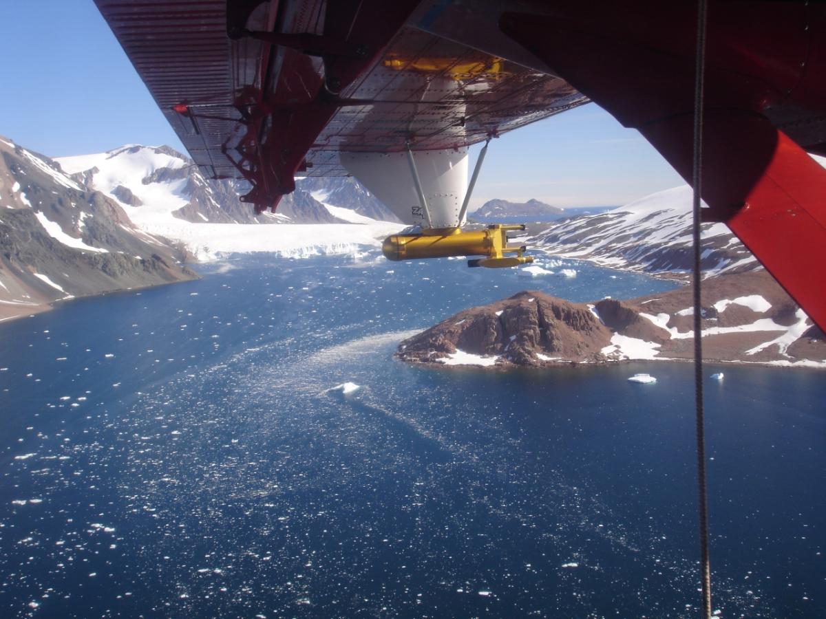 British Antarctic Survey Twin Otter aircraft with Cloud, Aerosol and Precipitation Spectrometer flying over mountainous coast in Antarctica.