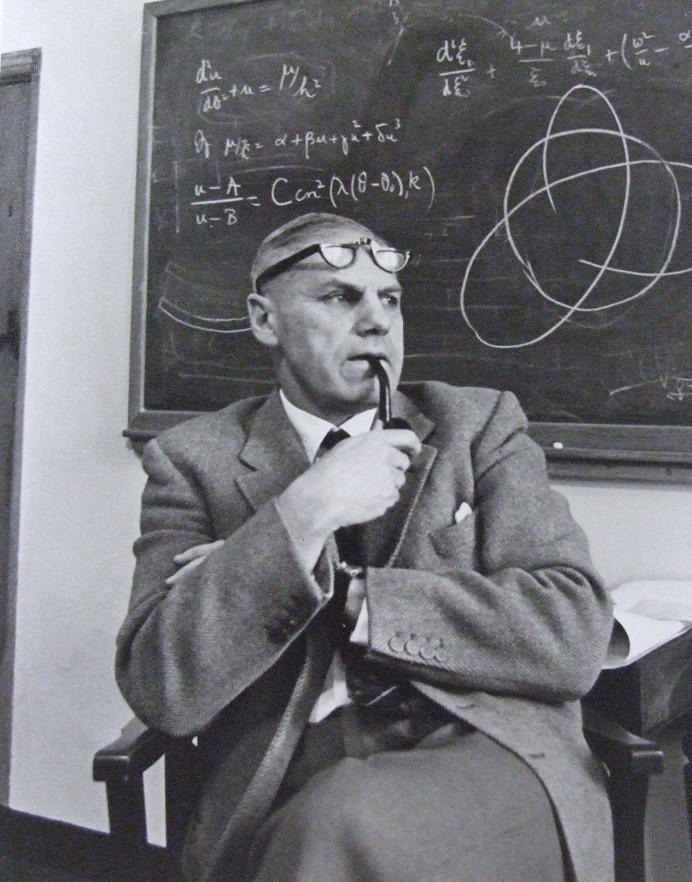 Photograph of Sir Richard van der Riet Woolley smoking a pipe in front of a blackboard with astronomy notes.