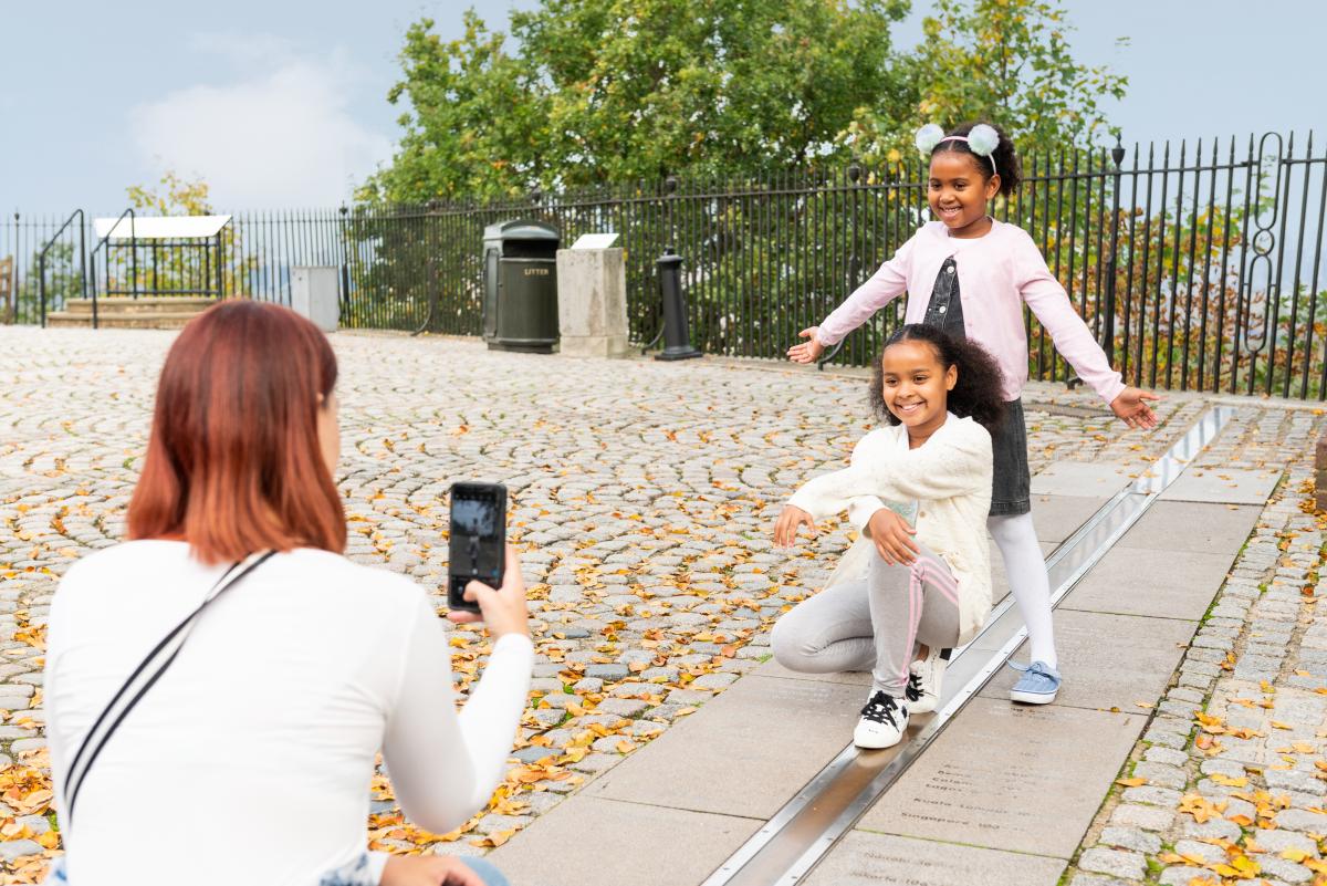 Woman taking photo with phone of two children at the meridian line