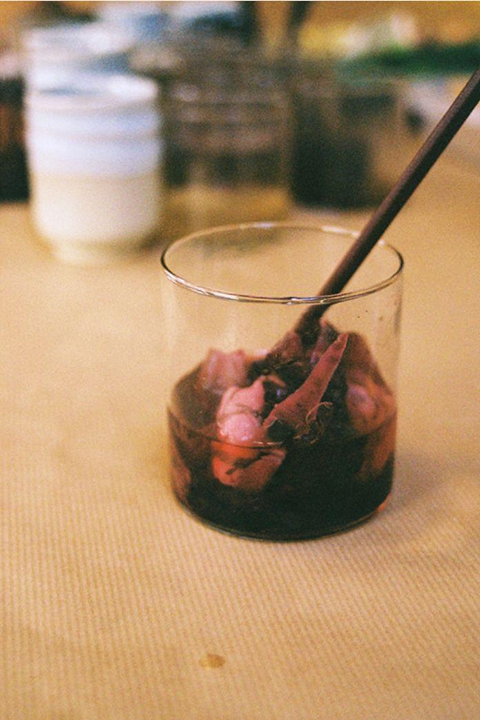 A beaker containing purple dye derived from tea, with a cloth and wooden spoon inside