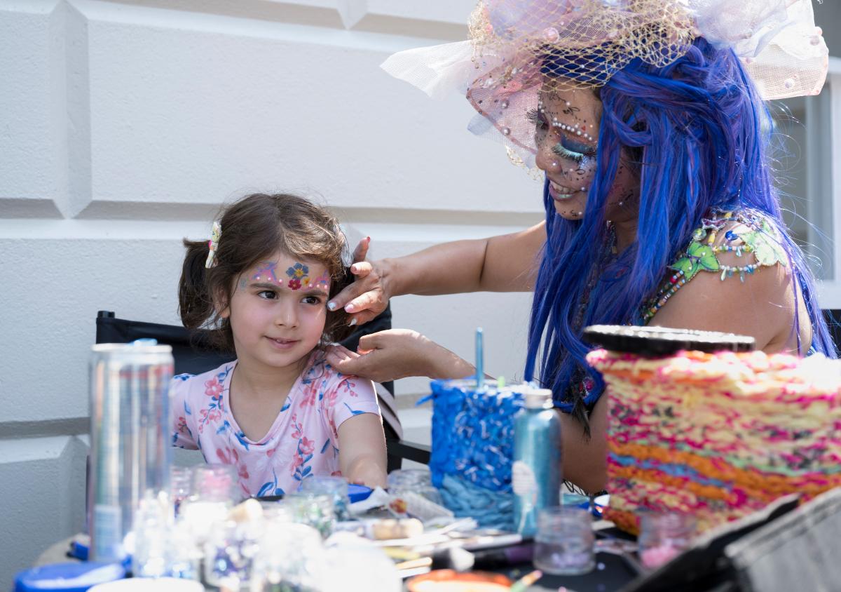 A young child has their face painted with glitter