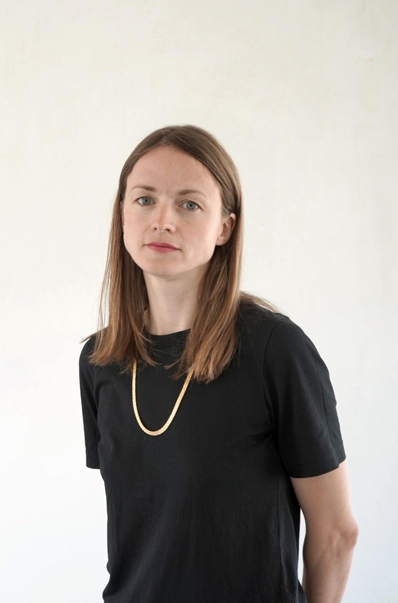 Portrait of Astrid Smitham facing at a 45 degree angle to the camera, wearing a black tshirt and a gold chain