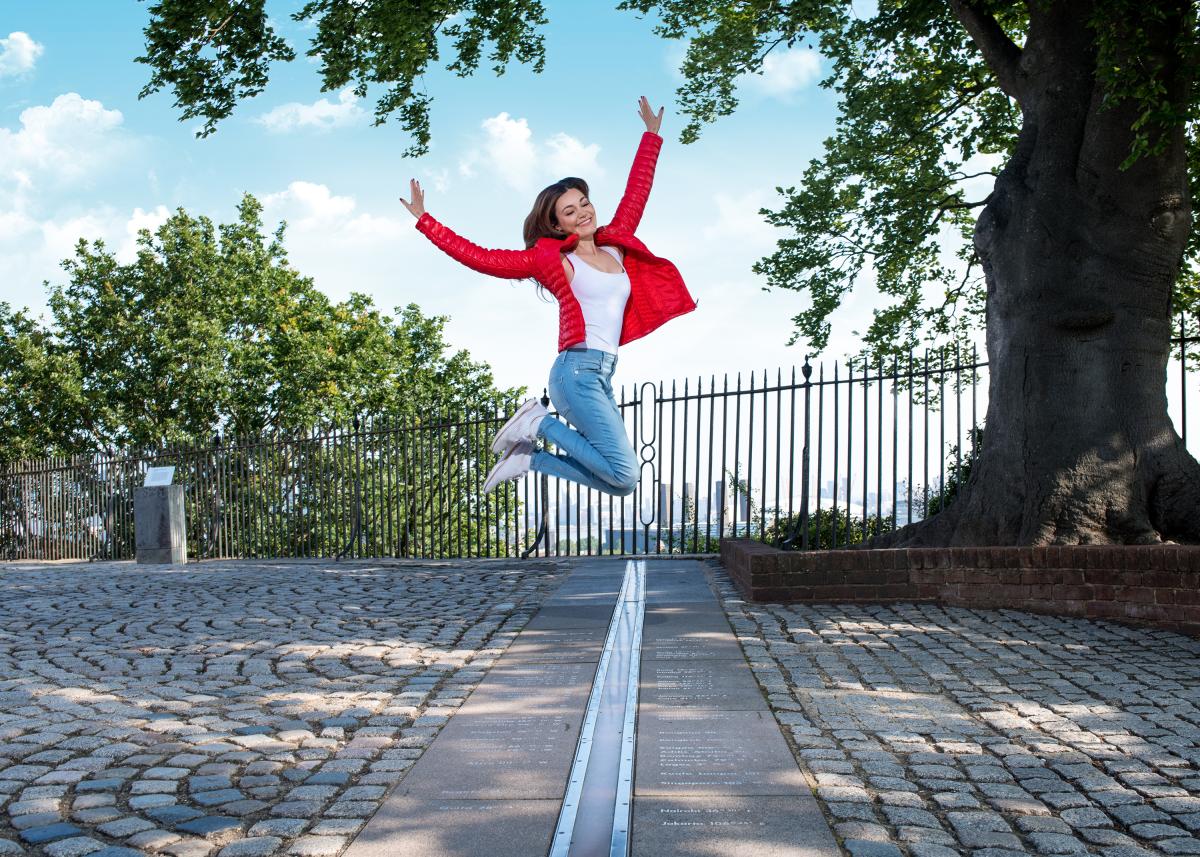 A woman in a red jacket leaps across the Prime Meridian Line at Royal Observatory Greenwich