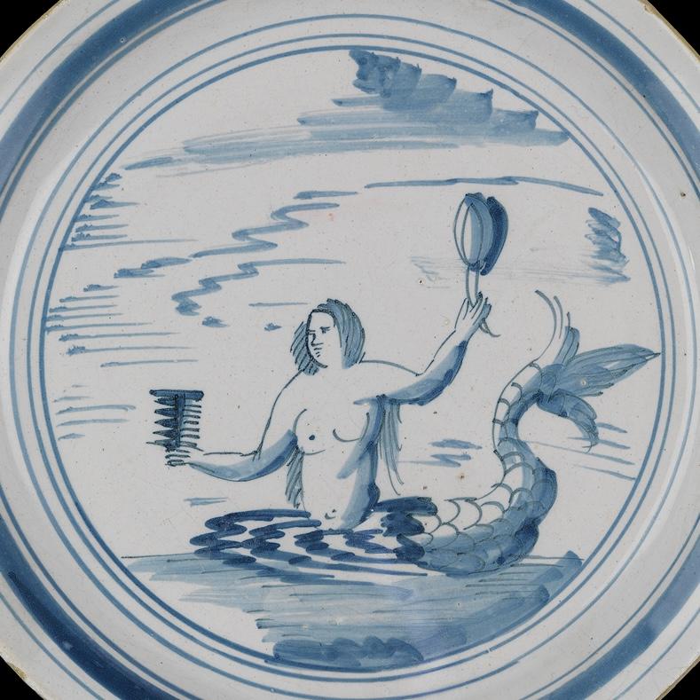 Tin-glazed, earthenware plate painted in blue with a mermaid holding a comb and a mirror