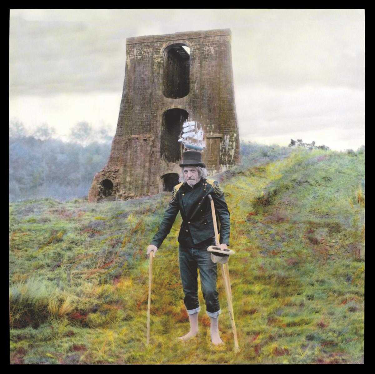 A man stands in heathland with the remains of a bridge behind