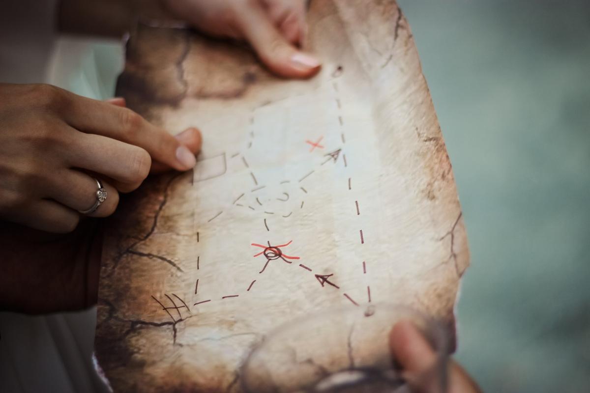 Two hands holding an old brown paper made to look like a treasure map